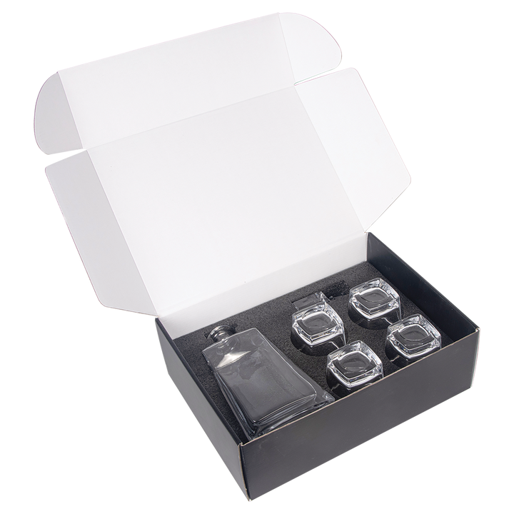 Open gift box containing clear glass decanter with stopper and four matching rocks glasses on black interior padding.