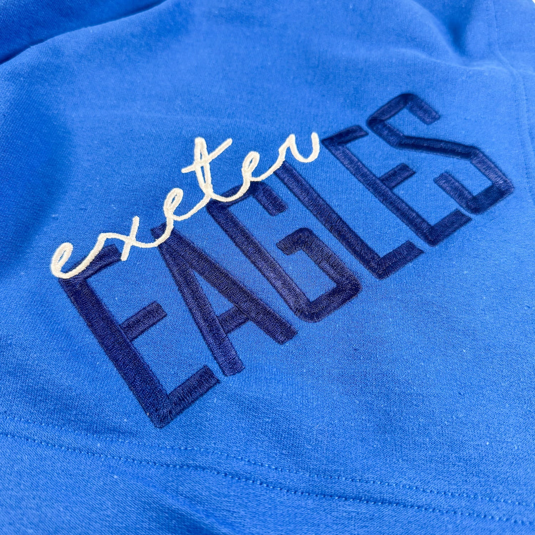 Royal blue fleece blanket with "exeter" in white script and "EAGLES" in navy block letters embroidered across the fabric