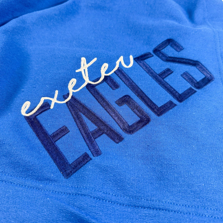 Royal blue fleece blanket with "exeter" in white script and "EAGLES" in navy block letters embroidered across the fabric
