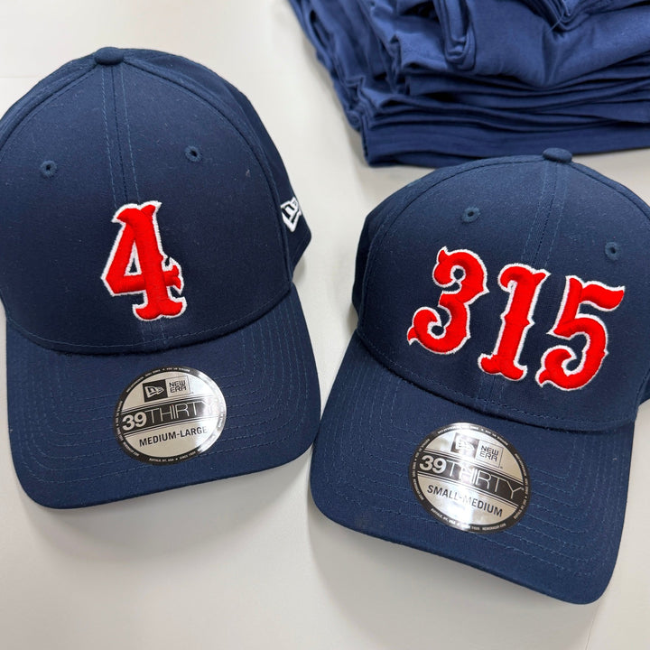 Two navy New Era stretch fit caps with red and white embroidered fire department numbers, factory size stickers still applied