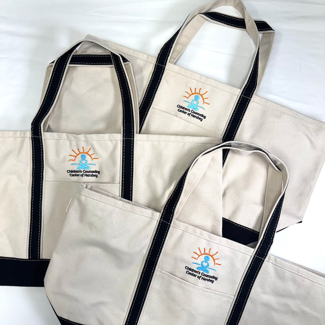 Three natural canvas tote bags with black handles and embroidered sun logo design on front pockets.
