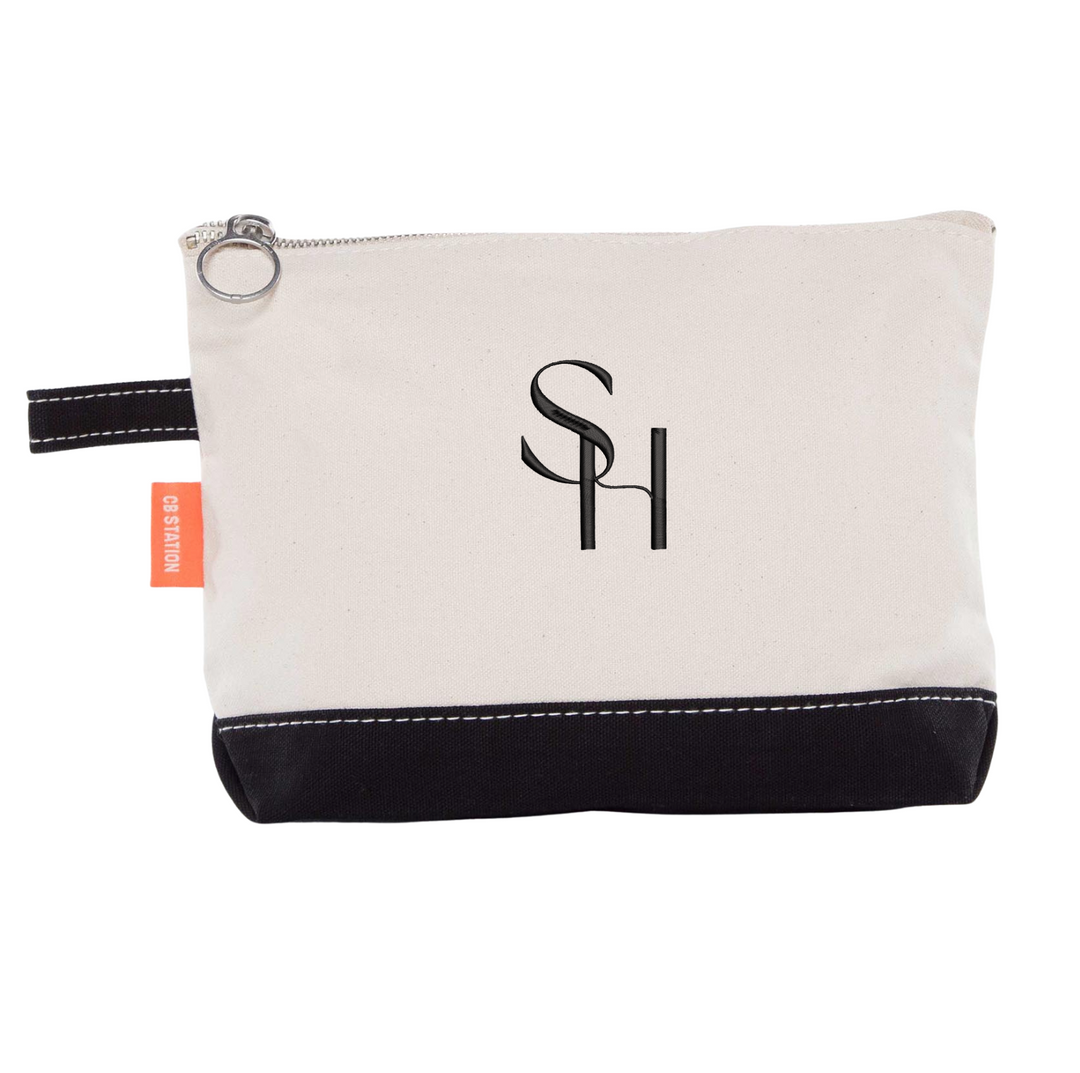 Canvas cosmetic bag with black bottom panel, silver zipper pull, and embroidered SH initials logo on cream fabric.