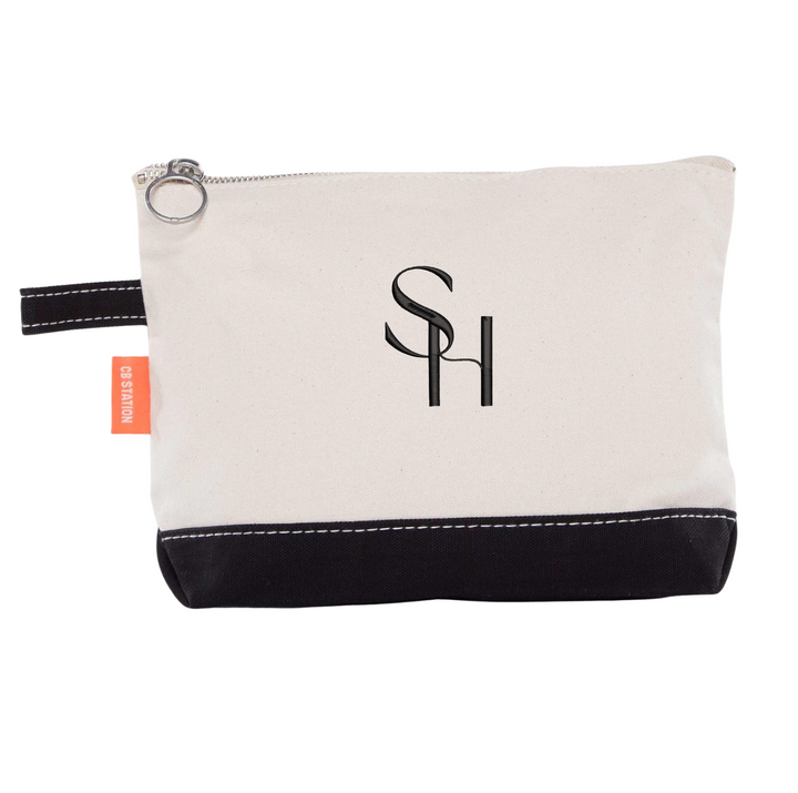 Canvas cosmetic bag with black bottom panel, silver zipper pull, and embroidered SH initials logo on cream fabric.