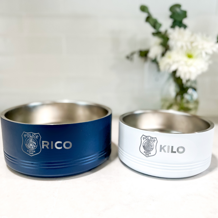 Blue and white stainless steel pet bowls engraved with police K9 unit names and department patches, displayed with flowers