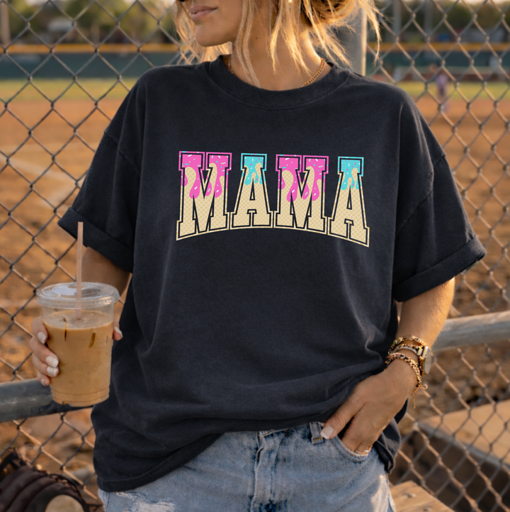 Mom at a baseball field wearing a black Baseball Mama t-shirt with a retro ice cream drip MAMA graphic, holding an iced coffee.