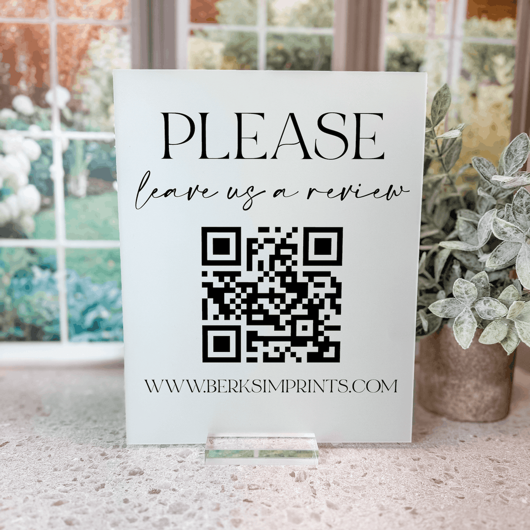 White acrylic tabletop sign with "PLEASE leave us a review" text, QR code, and www.berksimprints.com website address.