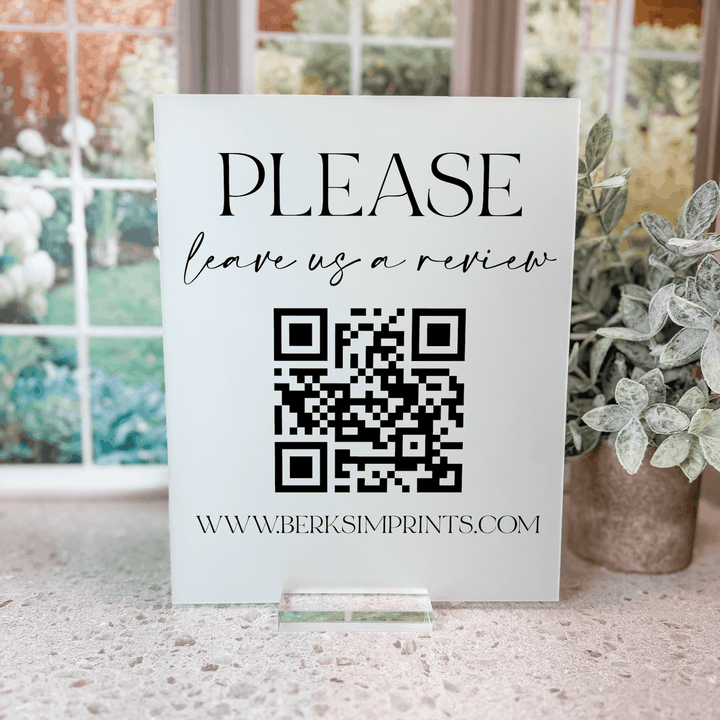 White acrylic tabletop sign with "PLEASE leave us a review" text, QR code, and www.berksimprints.com website address.