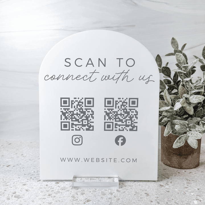 White acrylic arch-shaped table sign with QR codes and "Scan to connect with us" text, featuring Instagram and Facebook icons and website URL.