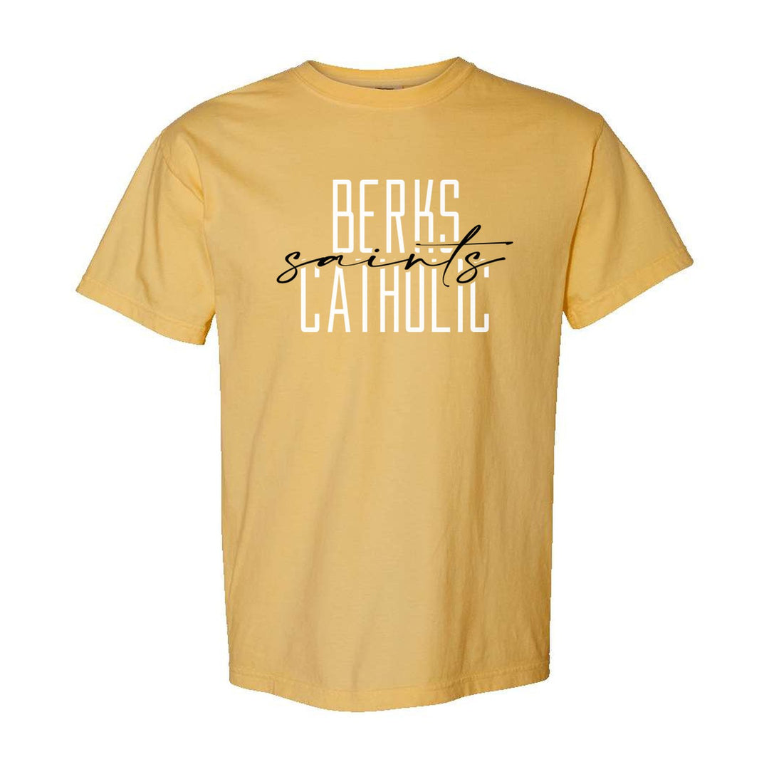 Berks Catholic Saints Tall Type Script comfort colors t-shirt in Mustard: tall BERKS CATHOLIC lettering with saints in flowing script across the middle