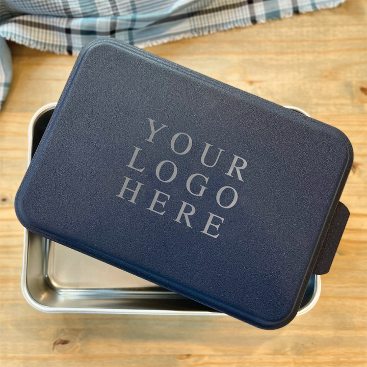 Dark blue neoprene cake pan carrier with "YOUR LOGO HERE" text, metal baking pan visible underneath on wooden surface.