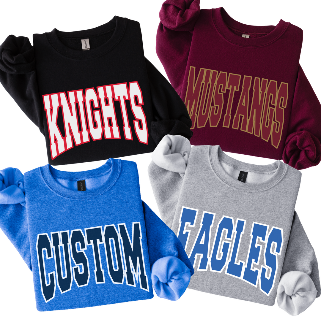 Four Gildan crewneck sweatshirts with arched varsity mascot lettering: black with red and white KNIGHTS, maroon with gold MUSTANGS, heather blue with navy CUSTOM, and sport grey with royal blue EAGLES